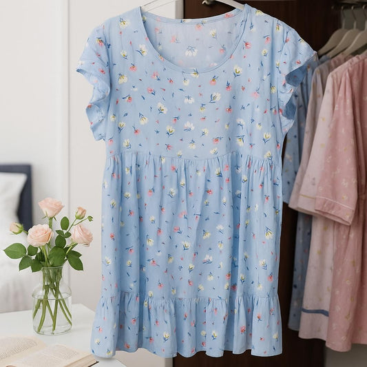 Light blue dress with floral pattern on a hanger, with a vase of flowers and another pink dress in the background.
